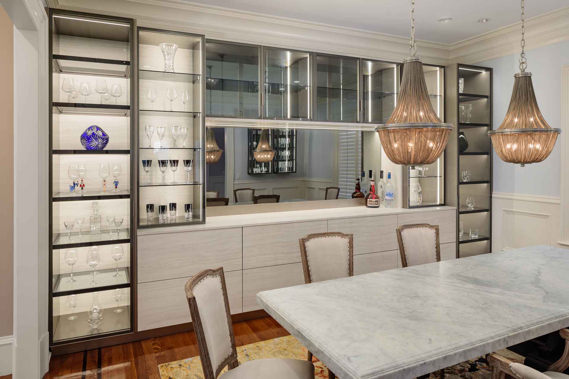 Elegant dining room with marble table, pendant lighting, and glass-fronted cabinets displaying glassware.