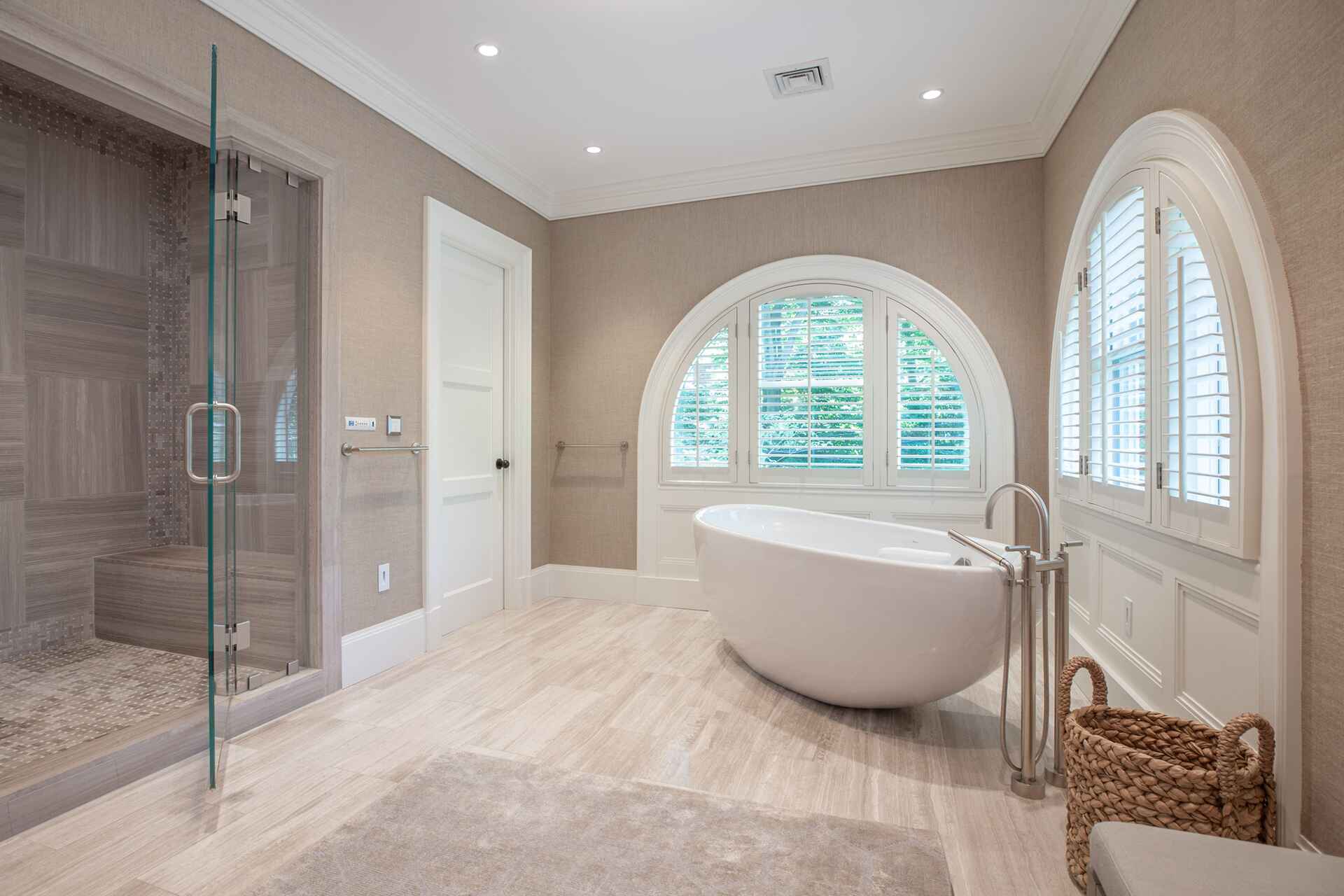 Luxurious bathroom with a freestanding tub, arched windows, and a glass-enclosed shower.