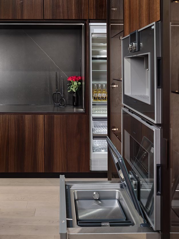 Sleek Boston kitchen with dark wood cabinetry, a black countertop, integrated sink, and modern built-in appliances.