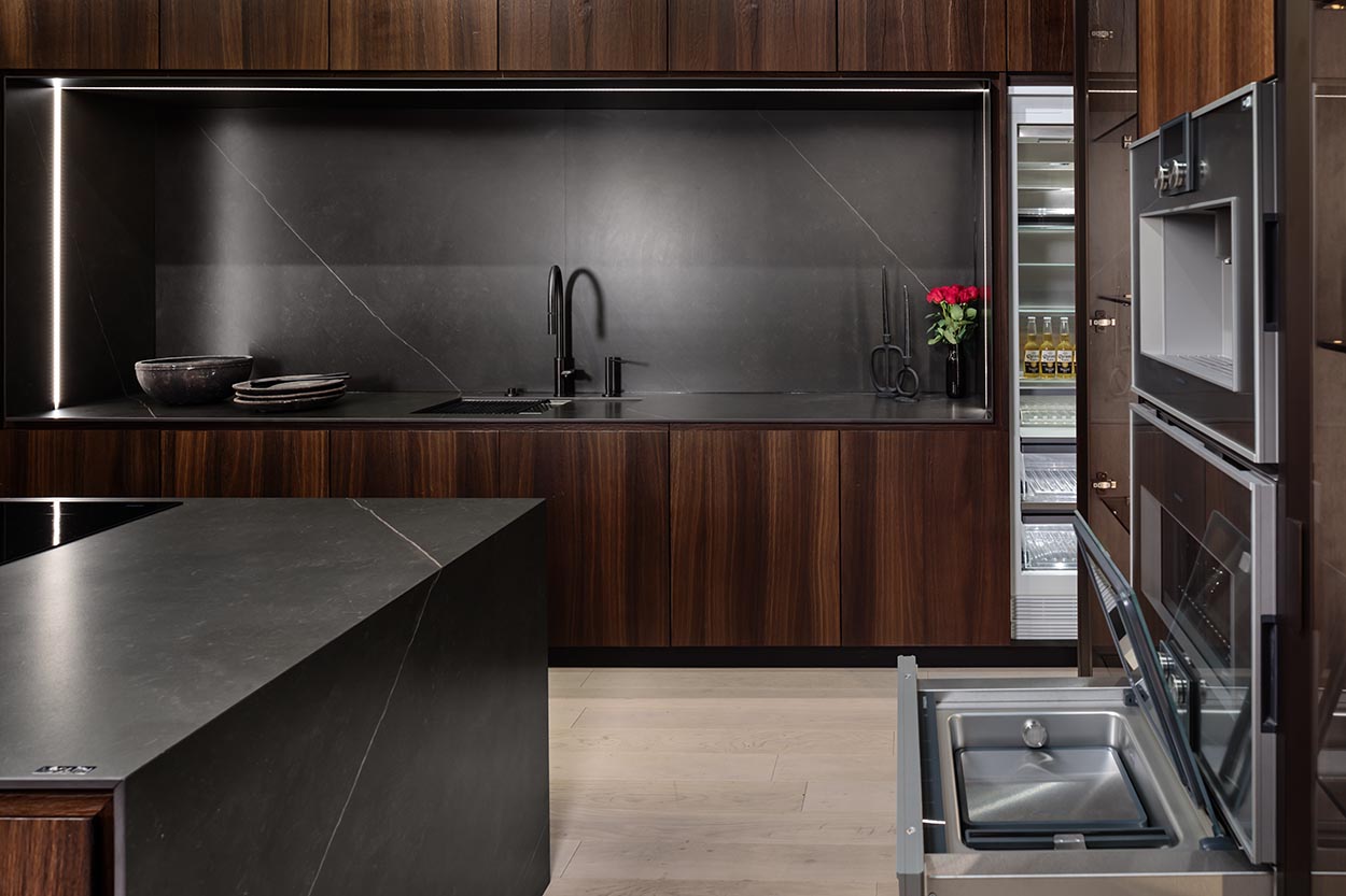 Sleek Boston kitchen with dark wood cabinetry, a black countertop, integrated sink, and modern built-in appliances.