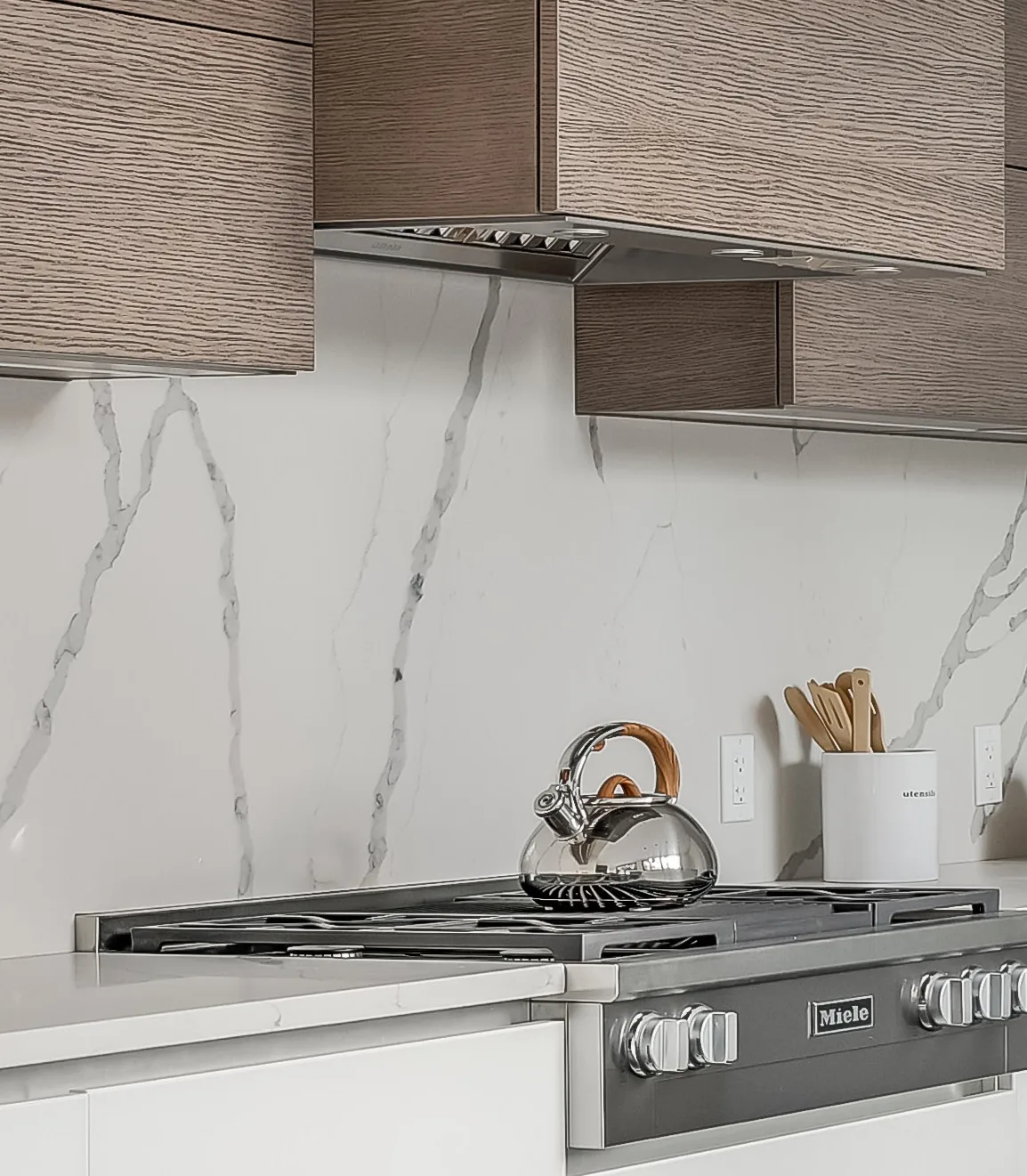 Stained oak kitchen cabinetry with pale stone backsplash in Wellesley