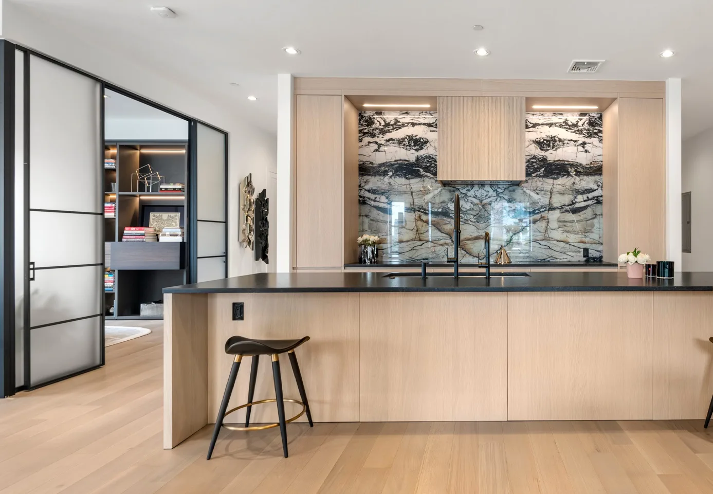 Wide kitchen view with pale oak cabinetry, charcoal island and veined natural stone in Boston