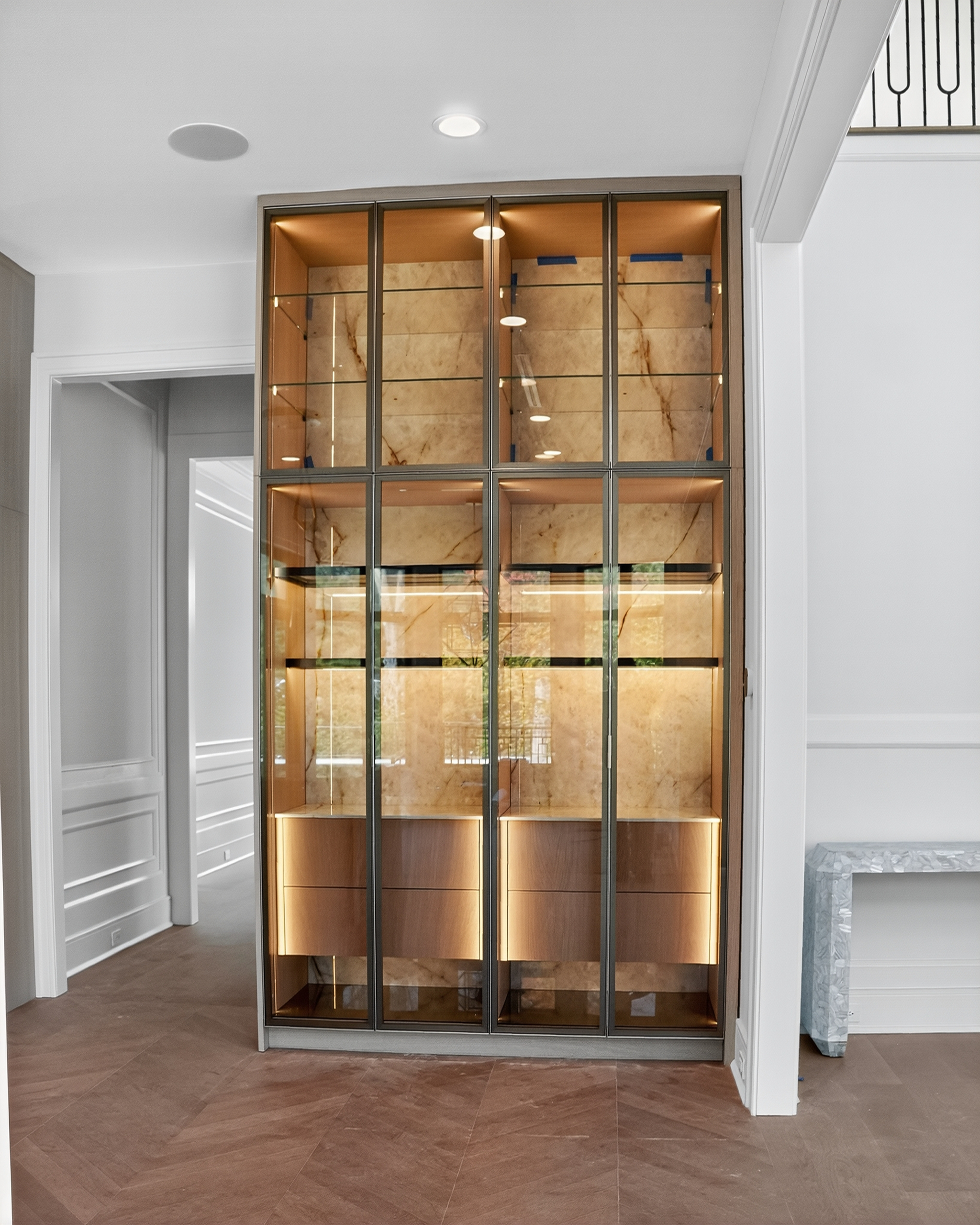 Illuminated glass display cabinet with warm wood drawers and veined stone backing