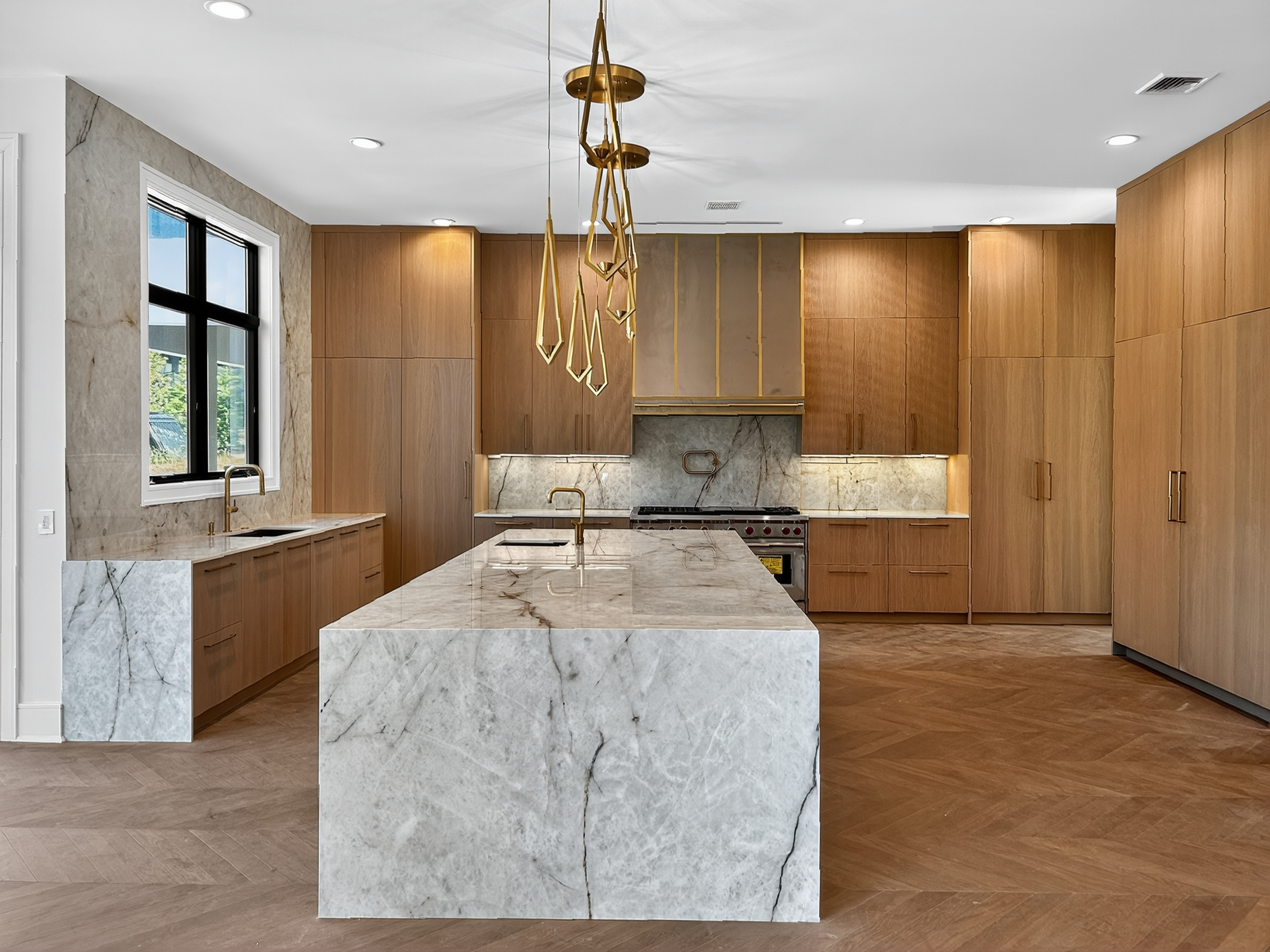 Luxury new-build kitchen with a veined stone island, warm wood cabinetry and brass-toned pendant lighting