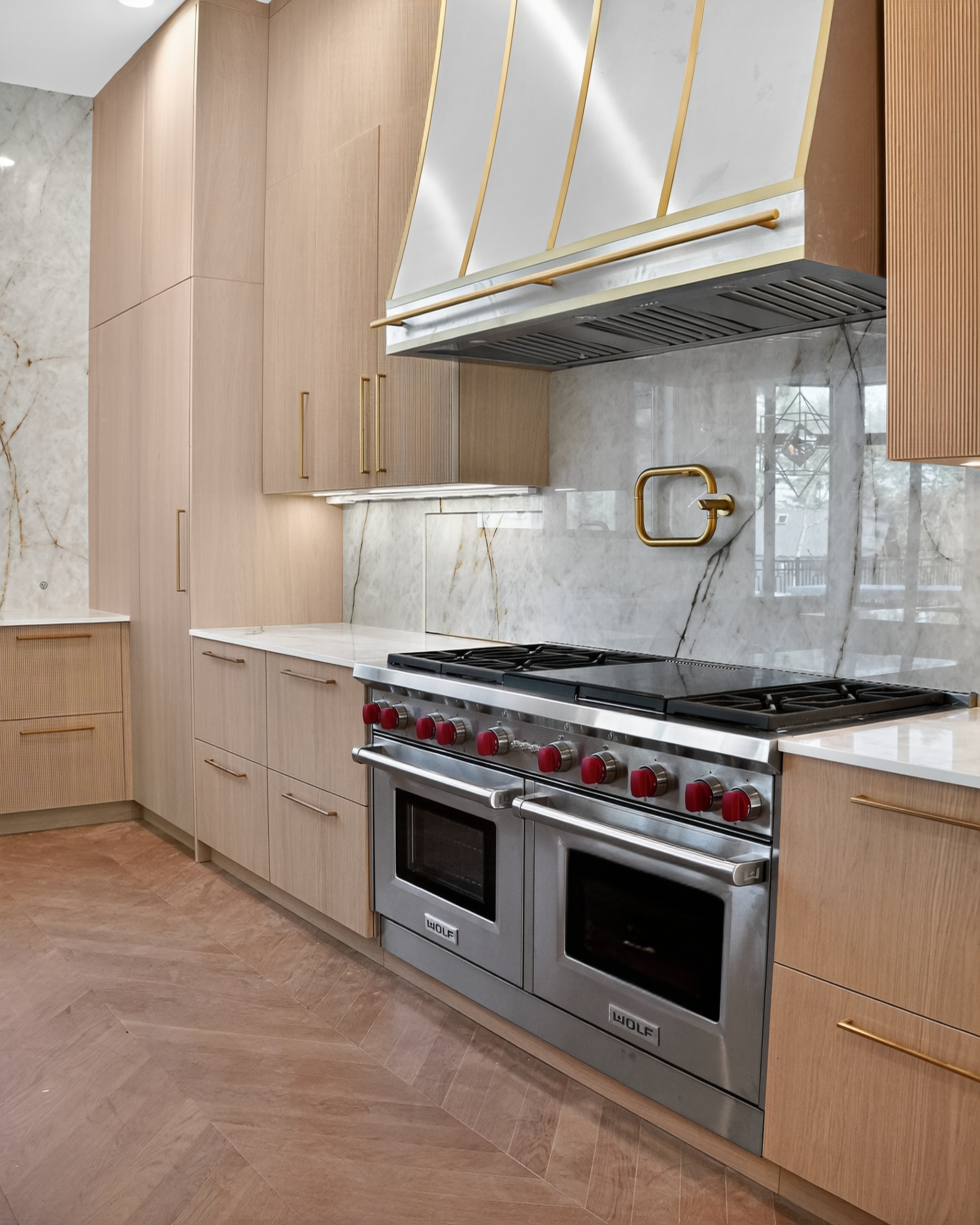 Range wall with veined stone, warm wood cabinetry and brass-toned hardware