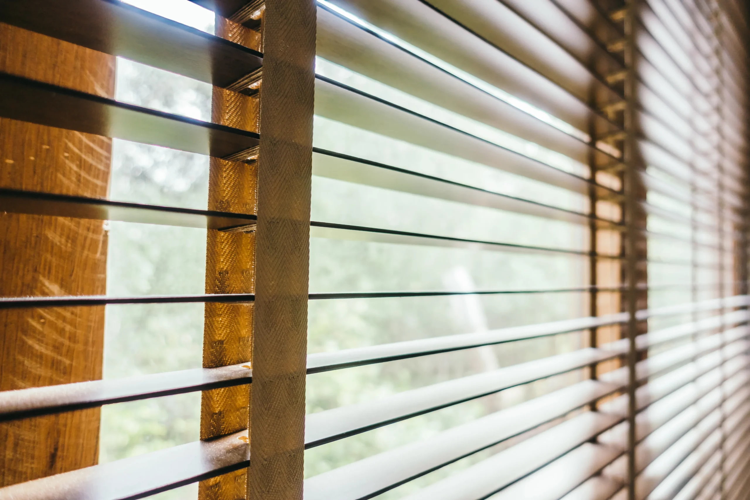 Close-up of wooden blinds with natural light filtering through, highlighting the texture and warmth of the wood.